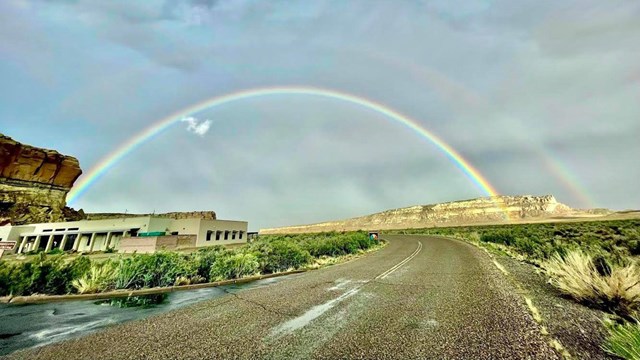A rainbow spanning the sky across a road next to a park visitor center.