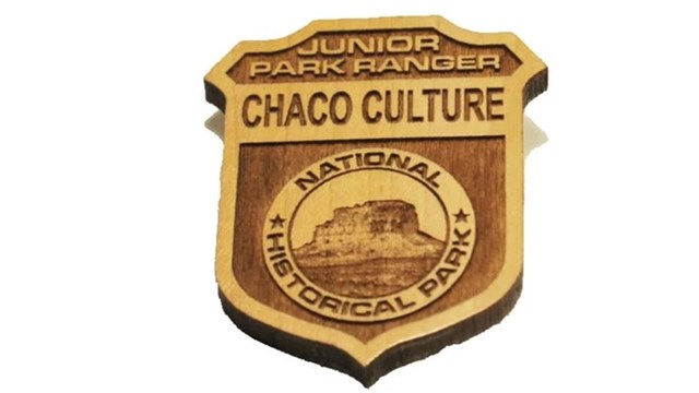 A wooden badge that says Junior Ranger Chaco Culture National Historical Park.