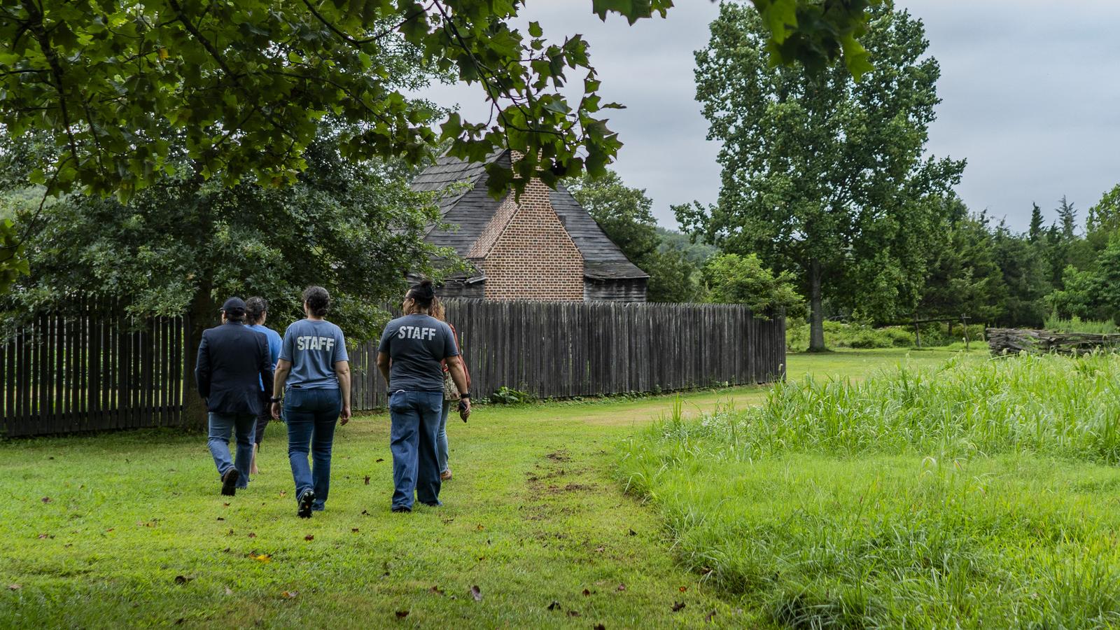 Staff members walking through a lush green landscape towards a brick building with a wooden fence.