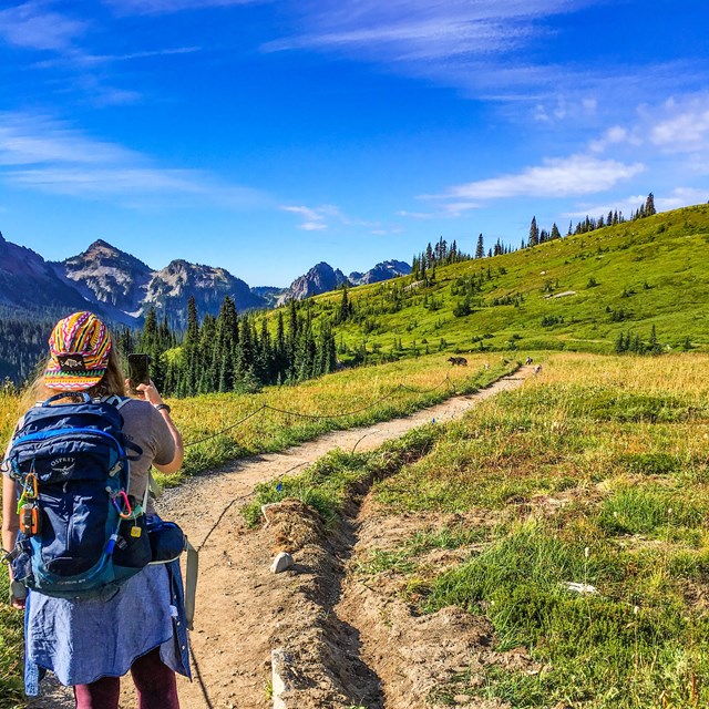 a hiker takes a photo with her phone while hiking on a trail in the mountains