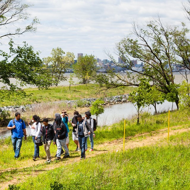 A group of students walk along a path near a small stream.