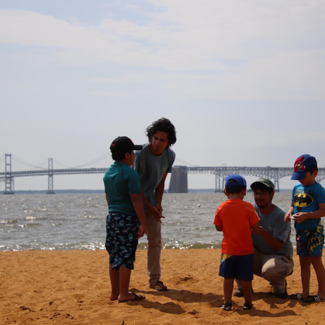 Three young boys speak with ranger interns on a sandy beach.