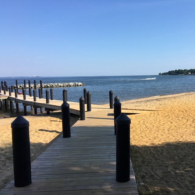 A dock extends from a sandy beach over water.