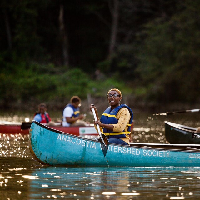 Two women paddle a bright blue canoe through water.