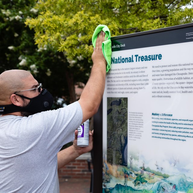 A man wipes down an interpretive sign titled 