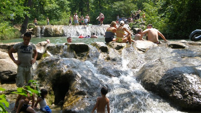a swimming hole and waterfall with dozens of people