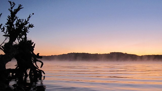 View of a lake with low hills in the distance at sunset.