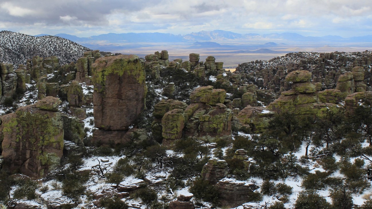 View down a canyon full of rock pinnacles, looking out across a valley. 