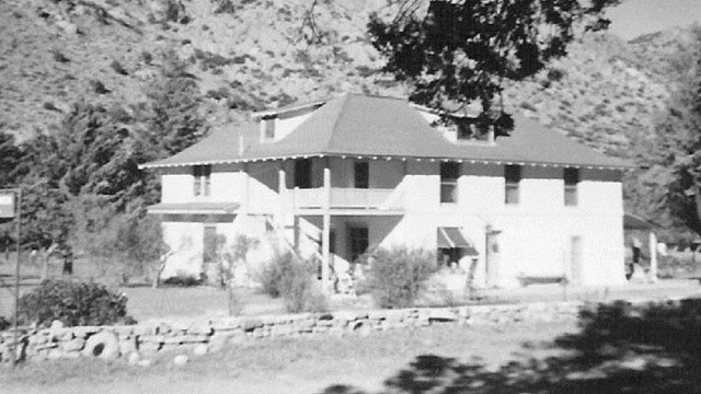 Black and white photo of a large square two-story house. 