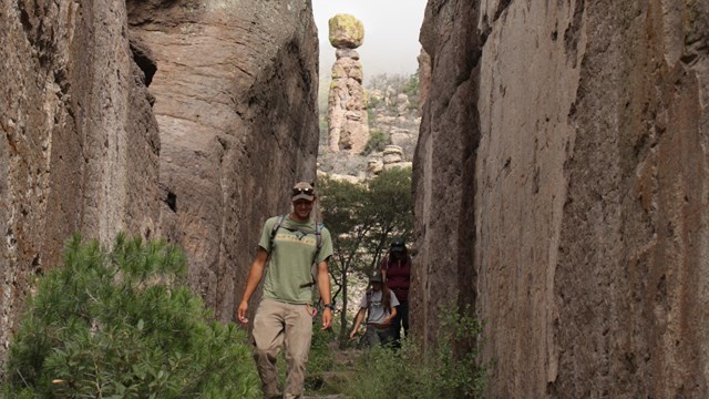 Hikers make their way through a narrow rock canyon