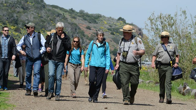 Ranger walking with press on dirt road. 