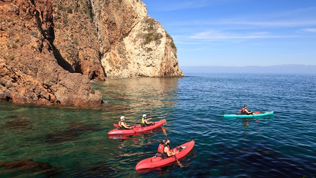 Kayakers in blue water next to steep cliff. ©Tim Hauf, timhaufphotography.com