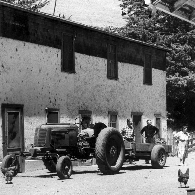 Rancher standing next to tractor in front of house. 