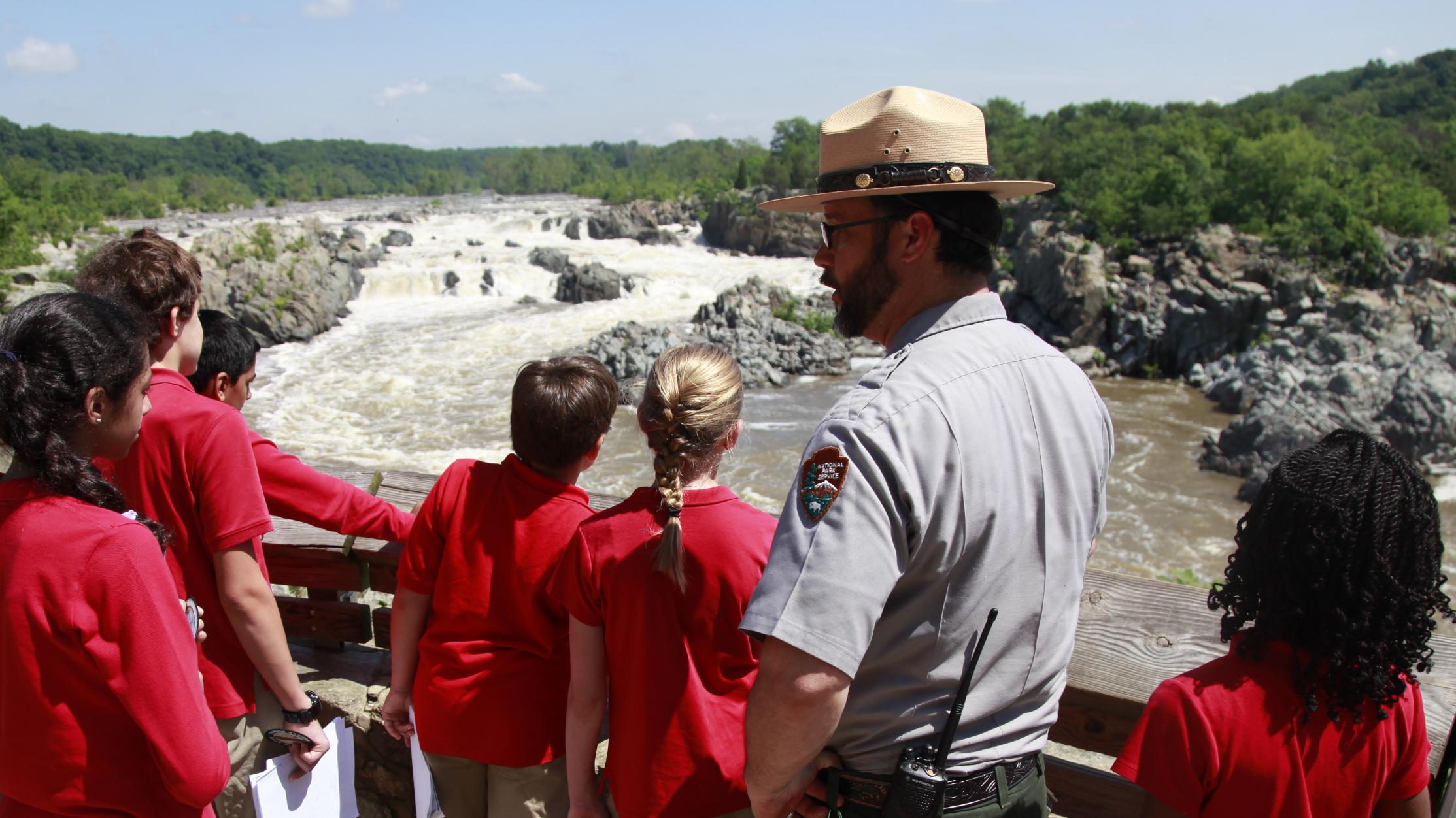 A group of children surround a park ranger in front of Great Falls