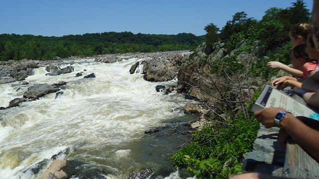 People's hand rest on railing while watching the Falls