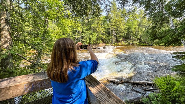 Child photographing a river in a forest.