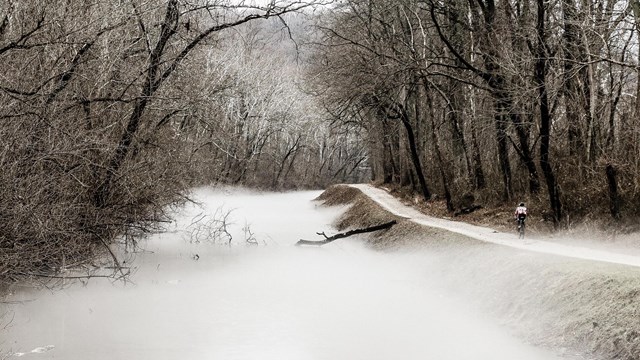 A biker rides along a mist filled canal.