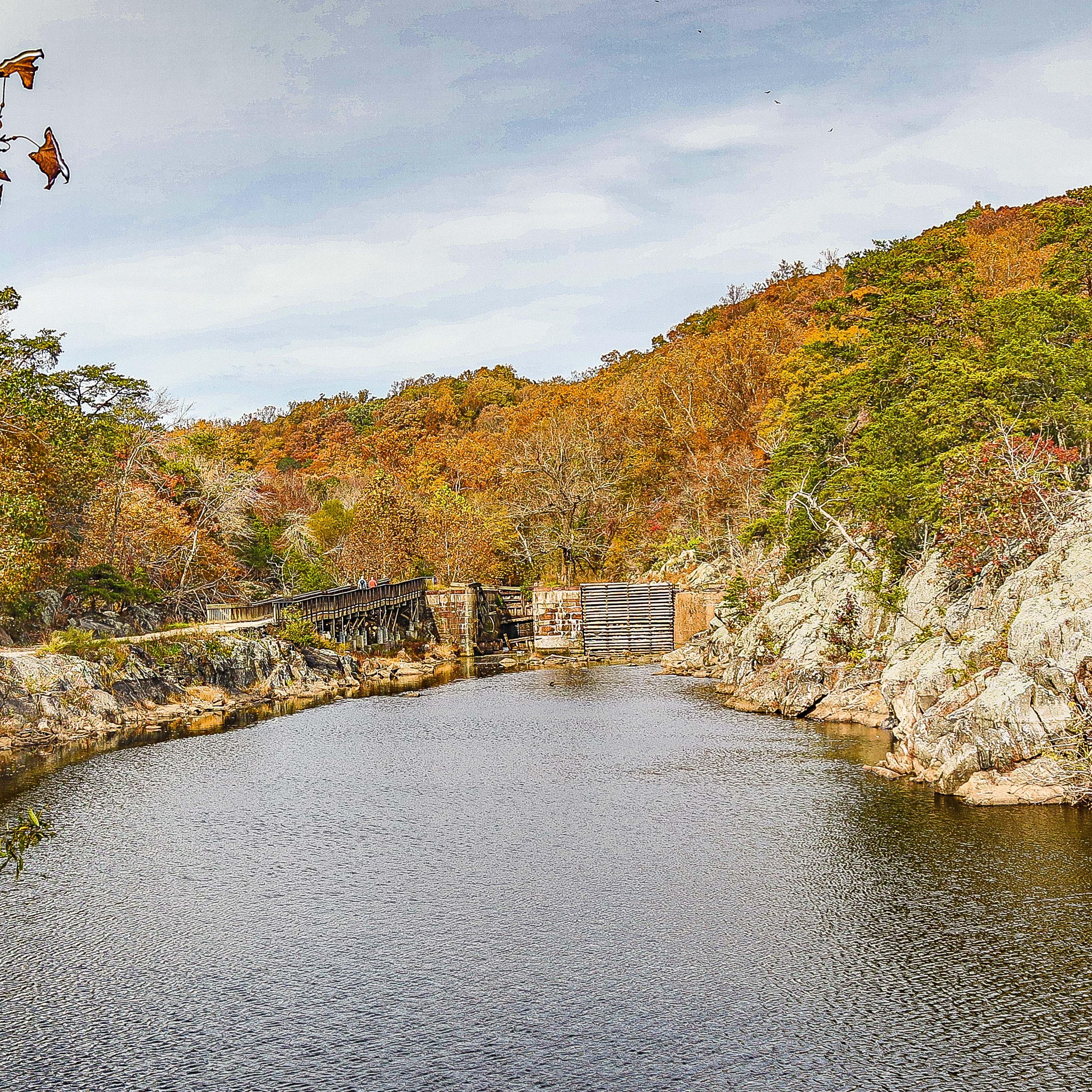 A rock wall and the towpath frame the canal leading to a large lock.