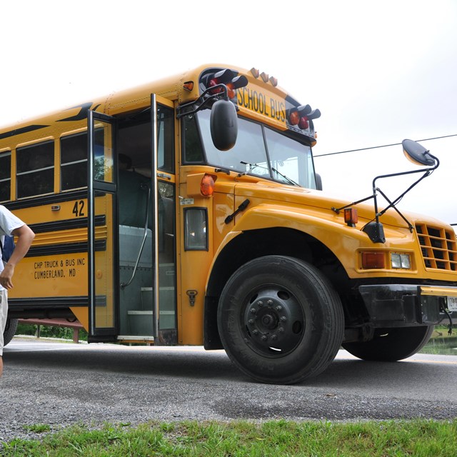 Ranger stands near school bus delivering students for field trip.