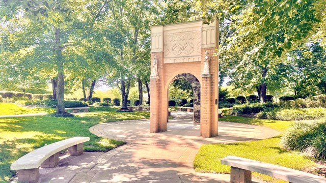 A view of the the site's Commemorative Garden with stone benches, trees and concrete arches.