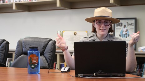 A ranger presents a virtual program on a laptop in the site's library.