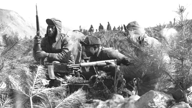 Black and white photo of 3 African American army soldiers in a machine gun emplacement.
