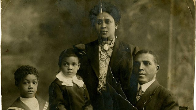 Black and white photo of African American Family posing for photo. There are 4 people in photo.