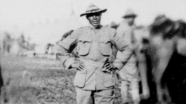 Charles Young, standing with hand on hips, next to horses and troopers