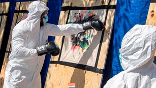 A man in a white jumpsuit uses boxing gloves to apply paint to artwork