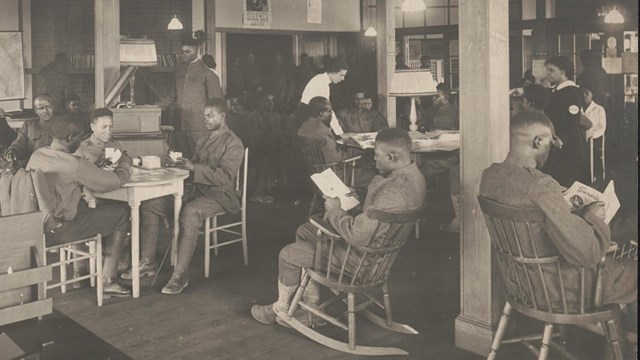African American male soldiers seated in a room reading while others stand in the background