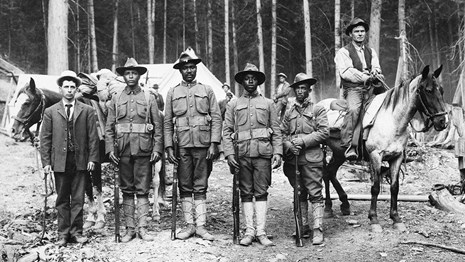 Black and white photo of 4 Buffalo Soldiers standing shoulder to shoulder in their fire camp in 1910