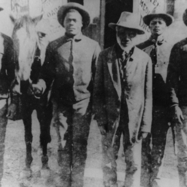 A row of Black soldiers standing at attention wearing wide-brimmed hats