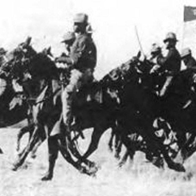 Several Black soldiers mounted on horses riding across a field