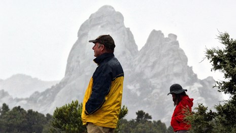 Two people in rain gear looking out over the landscape with misty granite spires in the backdrop.