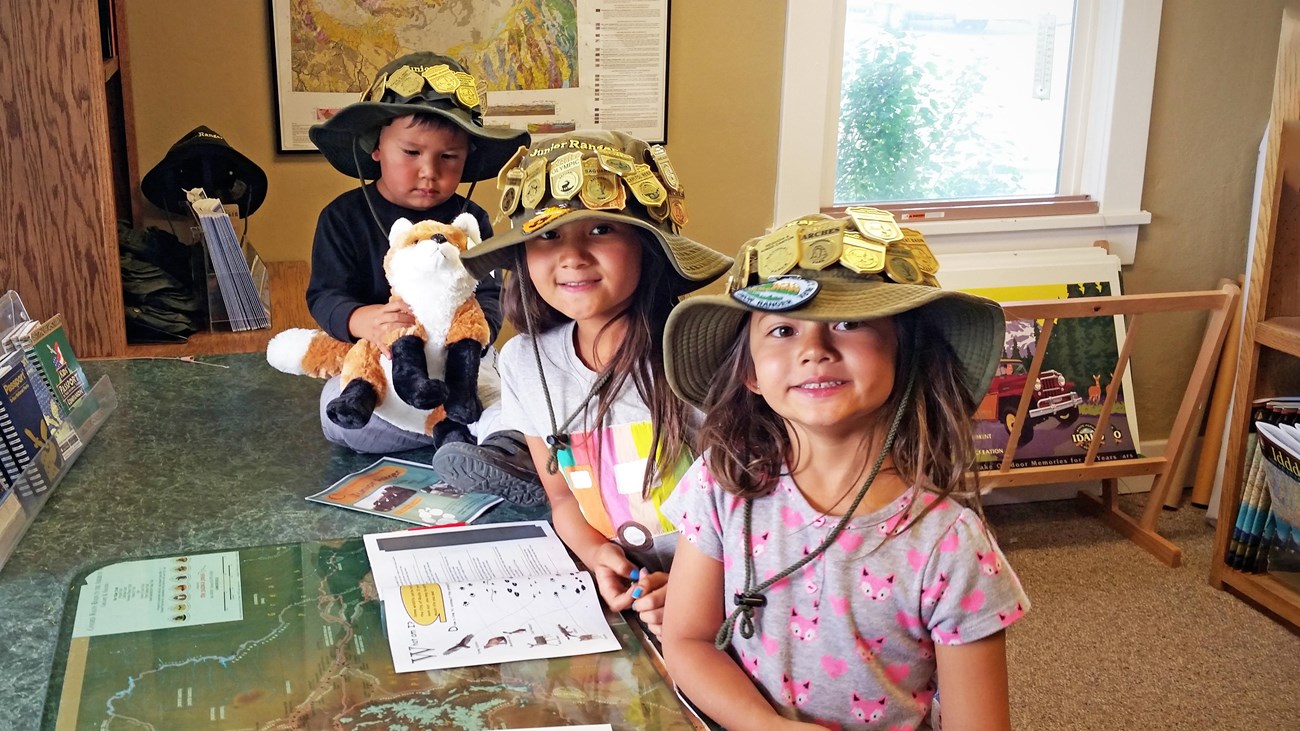 3 kids wearing bucket hats covered in junior ranger badges.