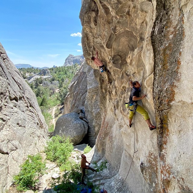 Two climbers on a granite wall, rock formations in the distance.