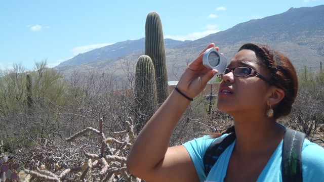 A woman looks through a measuring device in a desert landscape