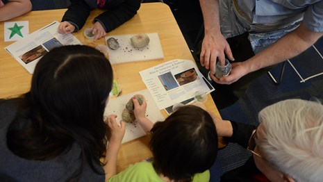Adults and children gather around a grinding stone