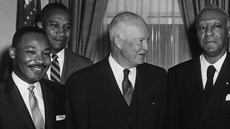 Black and white photo of Dr. King standing with line of men in black suits