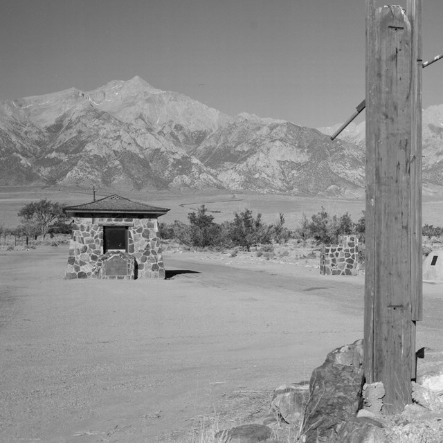 B&W, Wooden shack on left, two wooden posts in foreground, mountains in back