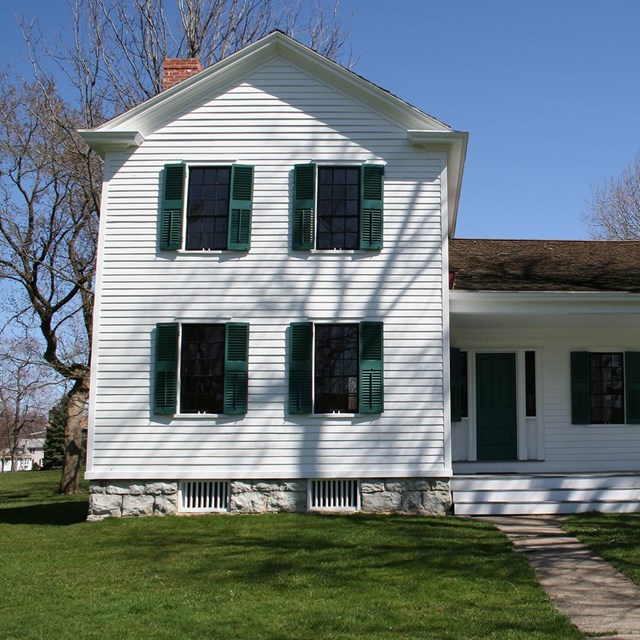 A white house with green shutters and green lawn