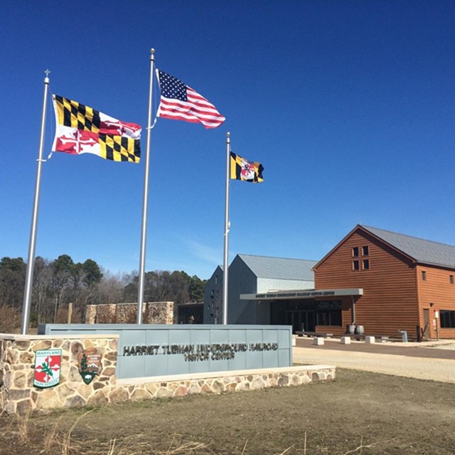 entrance sign with park name, flag poles, and two-story red brick visitors center