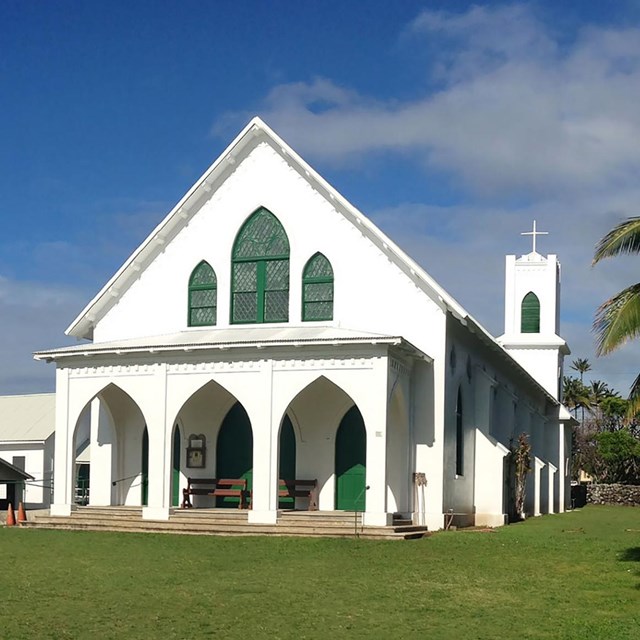 green grass with white church, blue sky, palm trees on right