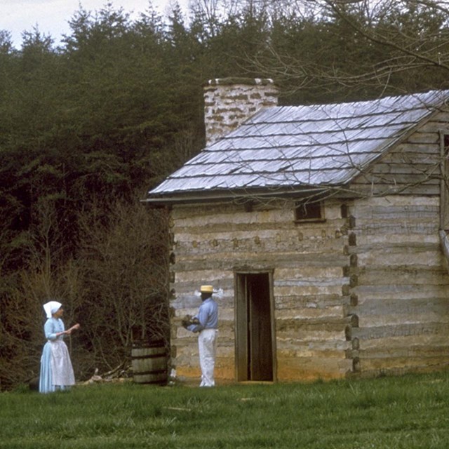 two people stand in front of a log cabin