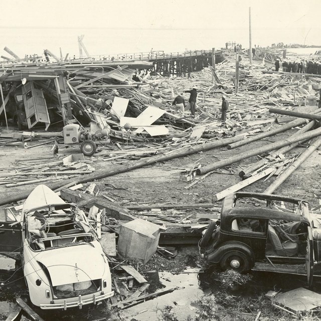 B&W; jumbled boards, cars and wooden poles