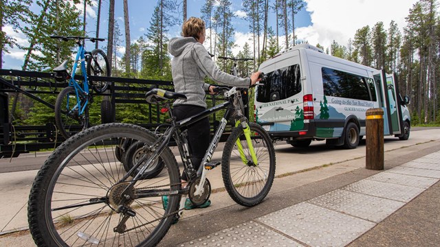 A cyclist prepares to load her mountain bike onto a trailer behind a shuttle van