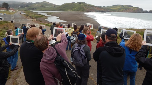 A crowd looks through transparent plastic windows at ocean beach on cloudy day