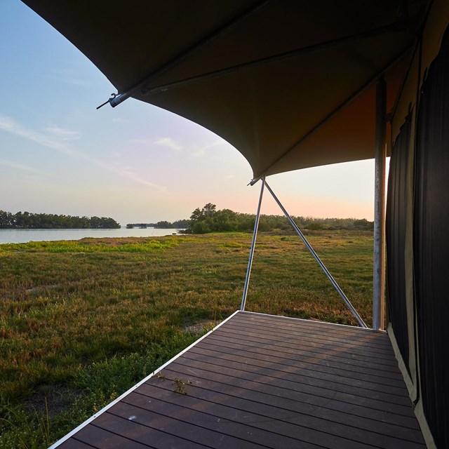 Looking out at grasses and a water inlet from a wooden porch with canopy overhead