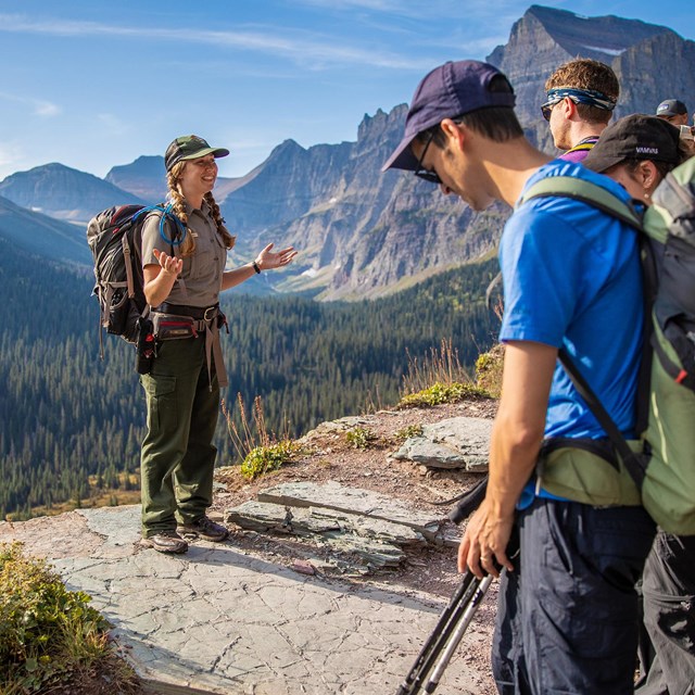 Park ranger speaks to a group of visitors while standing at viewpoint over a forested valley
