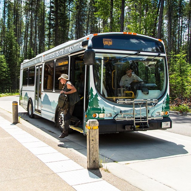 Passengers disembark a bus with a shelter and conifer forest in background 